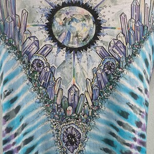 Puede incluir: Una camiseta tie-dye con un dise&ntilde;o de cristales coloridos y una imagen circular de un planeta en el centro.