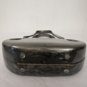 May include: A silver and black marbled clutch purse with a silver metal handle and a hinged closure. The purse has a unique, rounded shape and features clear plastic accents.
