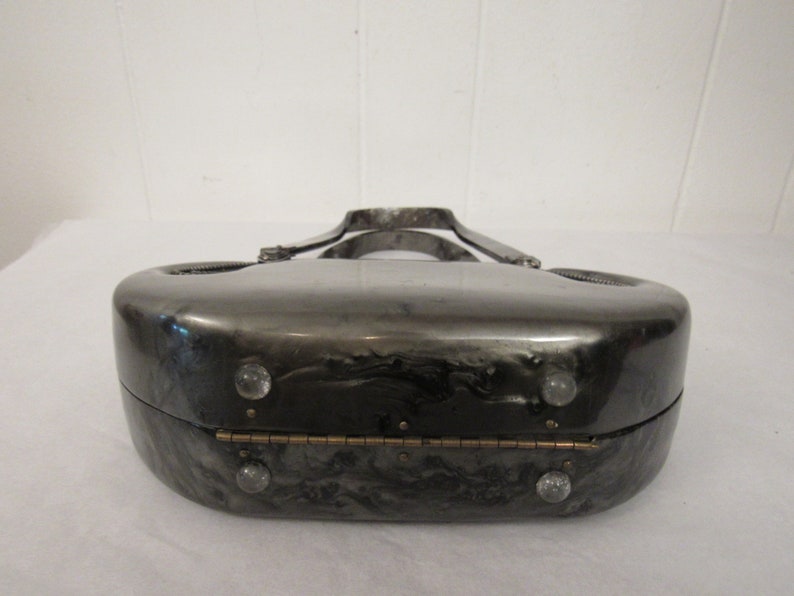 May include: A silver and black marbled clutch purse with a silver metal handle and a hinged closure. The purse has a unique, rounded shape and features clear plastic accents.