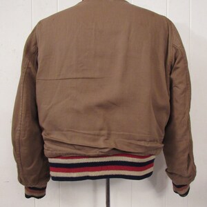 May include: A brown bomber jacket with a ribbed collar and cuffs. The cuffs have a navy, white, and red stripe pattern.
