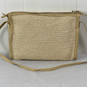 Könnte beinhalten: Eine beige gewebte Strohs Schultertasche mit einem Lederriemen und Besatz.