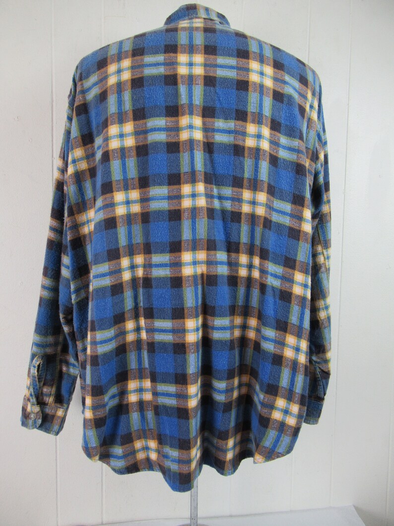 以下が含まれることがあります： 長袖でボタン留めの青い、黄色、茶色の格子柄のフランネルシャツです。