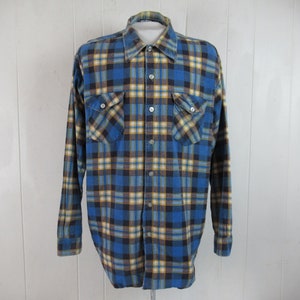 以下が含まれることがあります： 長袖で胸ポケットが2つ付いた、青、黄、黒のチェック柄のフランネルシャツです。