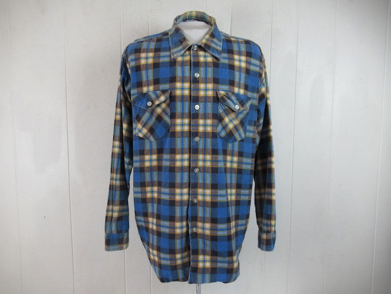 以下が含まれることがあります： 長袖で胸ポケットが2つ付いた、青、黄、黒のチェック柄のフランネルシャツです。