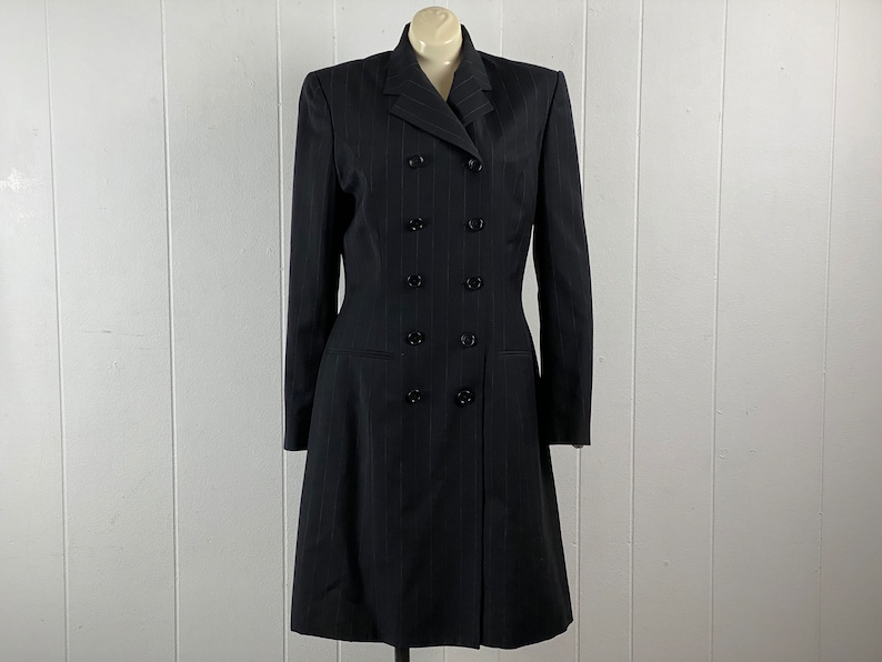 May include: A black pinstripe double-breasted coat with a long, fitted silhouette. The coat has a pointed collar and six black buttons down the front.