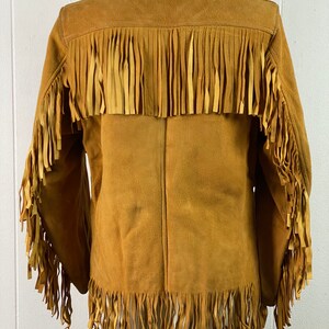 Puede incluir: Una chaqueta de gamuza marr&oacute;n con detalles de flecos en los hombros, las mangas y el dobladillo.