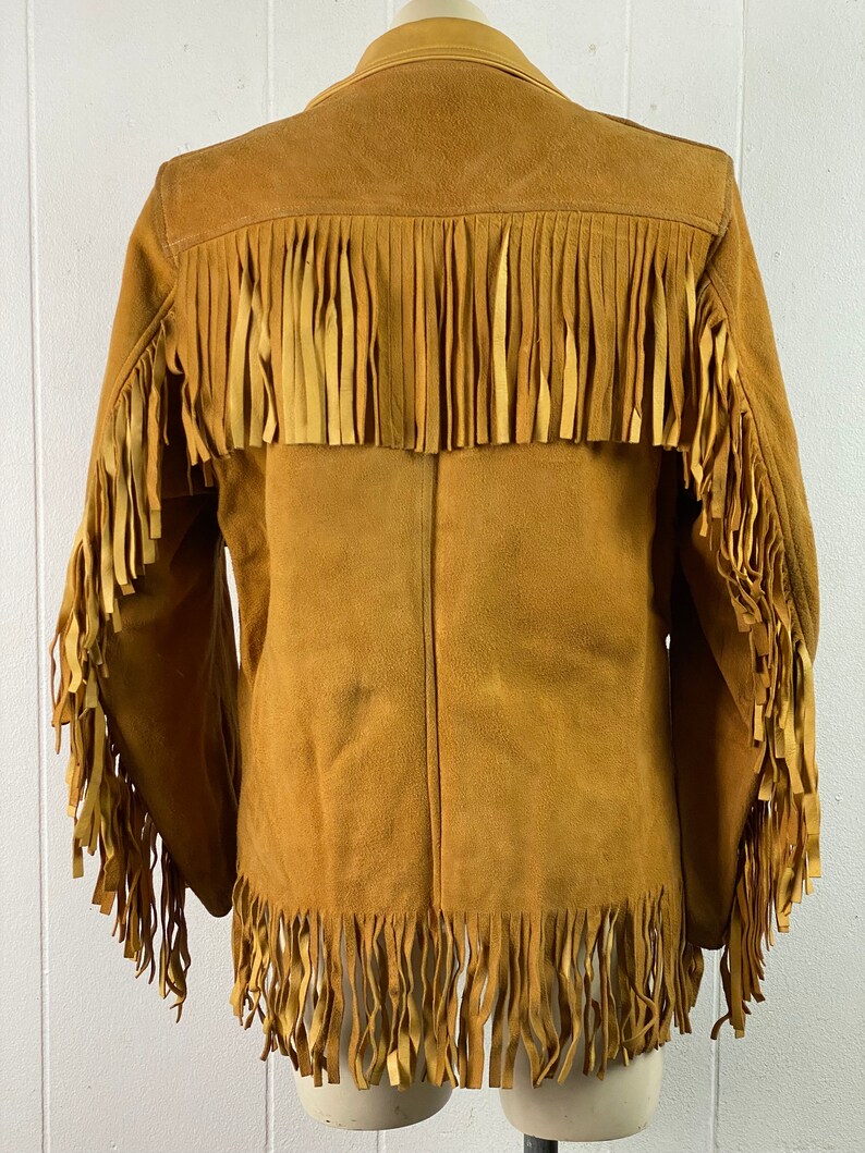 Puede incluir: Una chaqueta de gamuza marr&oacute;n con detalles de flecos en los hombros, las mangas y el dobladillo.