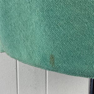 May include: A close-up of a green fabric with a woven texture. The fabric has a small brown stain.