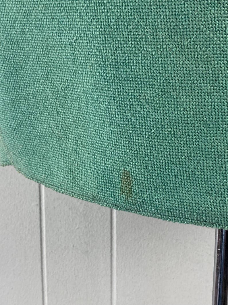 May include: A close-up of a green fabric with a woven texture. The fabric has a small brown stain.