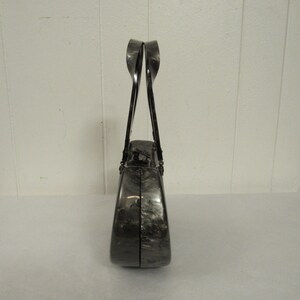 May include: A black and silver clutch purse with a unique, curved design. The purse has a top handle and a clasp closure.