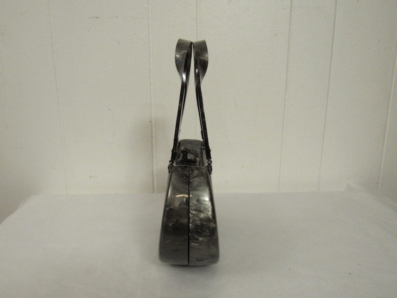 May include: A black and silver clutch purse with a unique, curved design. The purse has a top handle and a clasp closure.