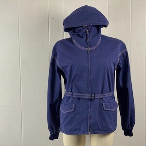May include: A blue hooded jacket with a white zipper and white stitching detail. The jacket has a belt and two pockets.