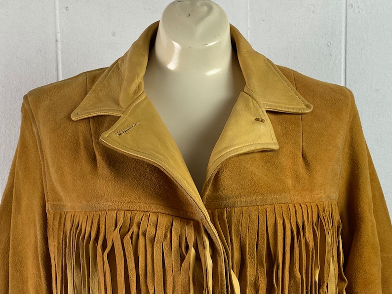 Puede incluir: Una chaqueta de ante marr&oacute;n con detalles de flecos. La chaqueta tiene cuello y cierre de bot&oacute;n.