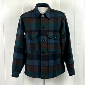 Peut inclure: Une chemise à manches longues boutonnée avec un motif à carreaux sombres dans des tons vert forêt, bleu marine et marron. La chemise comprend un col classique, deux poches poitrine à rabat boutonné et une fermeture boutonnée sur le devant.