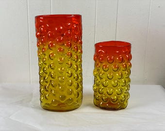 Könnte beinhalten: Zwei Glasvasen mit einem strukturierten Blasendesign. Die größere Vase ist gelb und orange, während die kleinere Vase gelb und rot ist.
