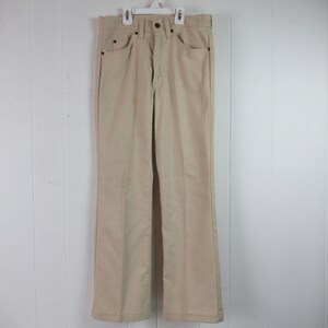 Peut inclure: Un pantalon beige à jambes larges avec une braguette à boutons et des passants de ceinture.