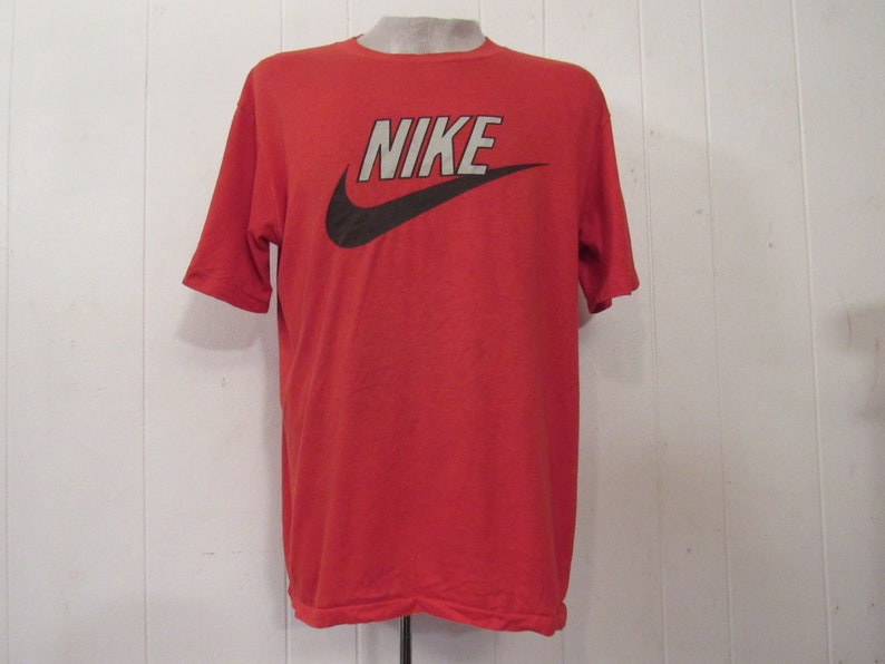 Puede incluir: Camiseta roja de manga corta con un logotipo de Nike en blanco y negro y la palabra "NIKE" impresa en la parte delantera.