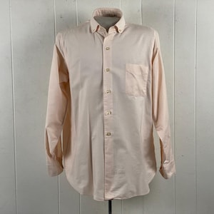 Op de afbeelding: Een lichtperzikkleurig overhemd met lange mouwen. Het overhemd heeft een button-down kraag, een borstzak en een gebogen zoom. Het overhemd wordt op een mannequin gepresenteerd tegen een witte achtergrond.