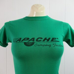 May include: Green short-sleeved t-shirt with a black print of "APACHE' Camping Trailers" with a stylized tire graphic.