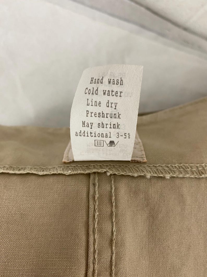 May include: Close-up of a beige fabric with a sewn seam and a care label. The label reads "Hand wash, Cold water, Line dry, Preshrunk, May shrink additional 3-5%."