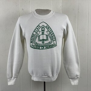 May include: White sweatshirt with a green emblem featuring the text "WAYNE STATE UNIVERSITY COLLEGE OF NURSING". The emblem includes a torch, an open book, and the words "INTELLIGENCE, INDUSTRY, INTEGRITY".