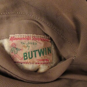 May include: A brown fabric jacket with a label that reads "Minnesota Inspired, Tailored by Butwin, Nationally Desired".