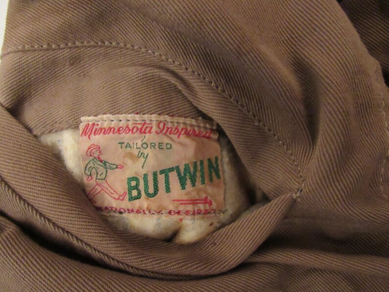 May include: A brown fabric jacket with a label that reads "Minnesota Inspired, Tailored by Butwin, Nationally Desired".