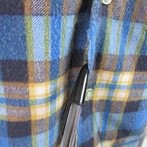 以下が含まれることがあります： 青、黄、茶色、白の格子柄のフランネルシャツのクローズアップ。シャツはボタン留めフロントと長袖です。