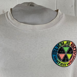 May include: White t-shirt with a colorful logo that says "Bugle Boy Water Wear" in a circle.
