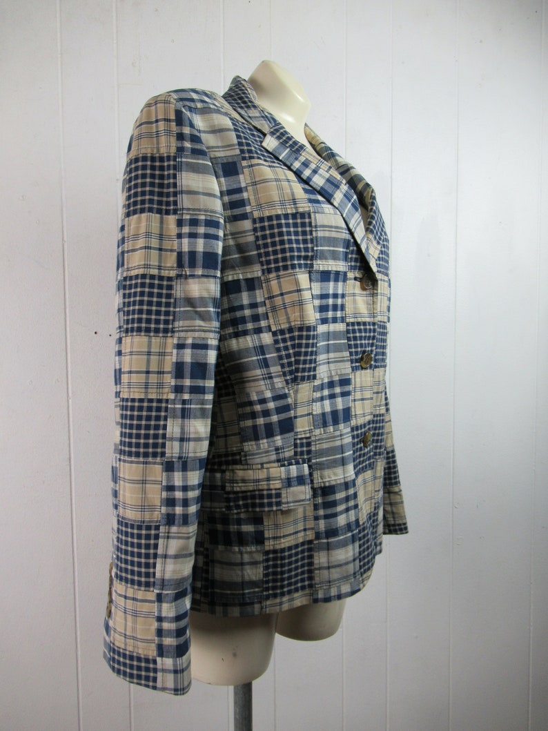 May include: A blue and beige plaid blazer with a patchwork design. The blazer has a notched collar, two button closure, and two flap pockets.