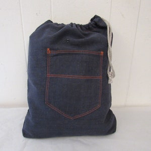 K&ouml;nnte beinhalten: Eine dunkelblaue Kordeltasche aus Denim mit einer gro&szlig;en, orangefarbenen, gesteppten Tasche auf der Vorderseite.