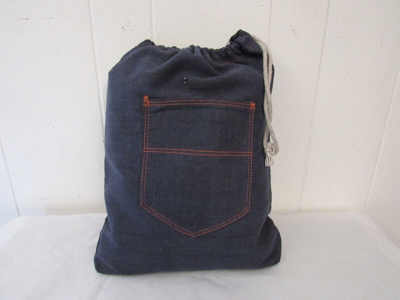 K&ouml;nnte beinhalten: Eine dunkelblaue Kordeltasche aus Denim mit einer gro&szlig;en, orangefarbenen, gesteppten Tasche auf der Vorderseite.