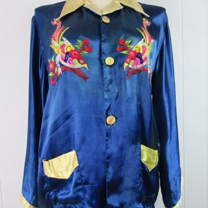 May include: A blue satin pajama set with gold trim and embroidered birds. The jacket has a collar, button closure, and two pockets. The pants have a straight leg.
