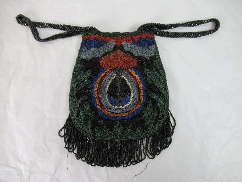 Puede incluir: Un bolso de cuentas negras con un fondo de flecos. El bolso tiene un dise&ntilde;o colorido con cuentas verdes, azules, rojas y naranjas.