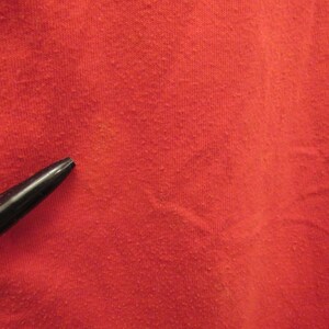 Puede incluir: Primer plano de una tela roja con una superficie texturizada. Un bol&iacute;grafo negro est&aacute; sobre la tela.