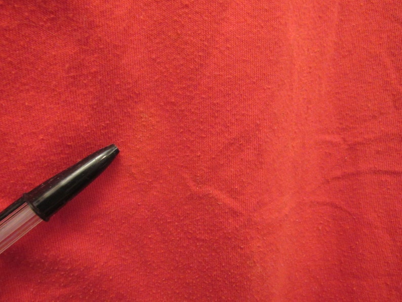 Puede incluir: Primer plano de una tela roja con una superficie texturizada. Un bol&iacute;grafo negro est&aacute; sobre la tela.