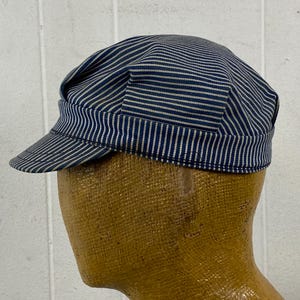 May include: A blue and white striped cap with a short peak. The cap is made of a fabric with vertical stripes. The cap is worn on a mannequin head. The cap is a classic style.