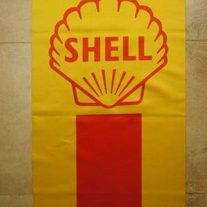Puede incluir: Una pancarta amarilla y roja con el logotipo de Shell. El logotipo es una concha estilizada roja con la palabra "SHELL" en letras rojas.