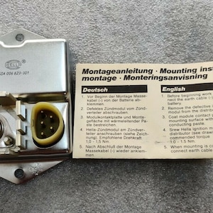 Può includere: Un modulo di accensione per auto in argento con un foglio di istruzioni in bianco e nero. Il foglio contiene istruzioni in tedesco e inglese. Il modulo ha il numero di parte 504 006 621-301.