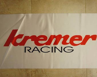 Puede incluir: Bandera blanca con texto rojo que dice "kremer RACING" en una fuente estilizada.