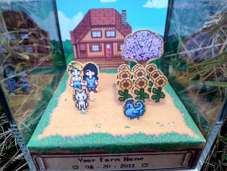 May include: A diorama featuring a pixelated farm scene with a house, sunflowers, and characters. The scene includes a cat, a blue bird, and two people. The base of the diorama has text that reads "Your Farm Name" and a date.