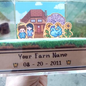 May include: A pixelated diorama featuring a farm scene with a house, characters, and sunflowers. The text "Your Farm Name" and the date "08-20-2011" are displayed on a banner at the bottom. The scene is set inside a clear display case.