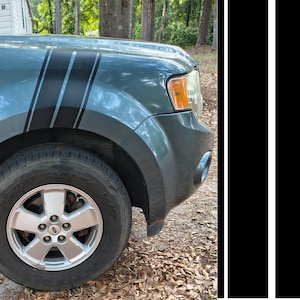 May include: A teal car fender with black racing stripes. The car has a silver wheel with a black tyre. The background includes trees and a house.