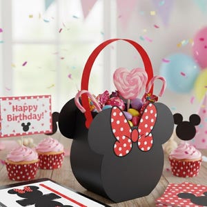 May include: A black Minnie Mouse-shaped gift basket with a red handle and bow, filled with candy and a heart-shaped lollipop. The scene includes cupcakes, a "Happy Birthday" sign, and confetti, perfect for a party.