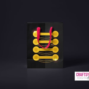 May include: Black shopping bag with a red handle and a gold geometric design. The bag has a shiny, metallic finish.