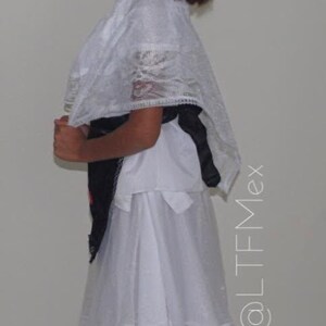 May include: A white dress featuring a sheer lace overlay with intricate patterns, a scalloped hem, and a black sash tied at the waist. The garment includes a matching white lace shawl draped over the shoulders. The text @LTFMex is visible.