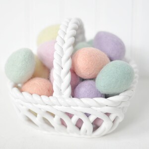 May include: A white ceramic basket filled with pastel colored felt Easter eggs. The basket has a braided rope handle.