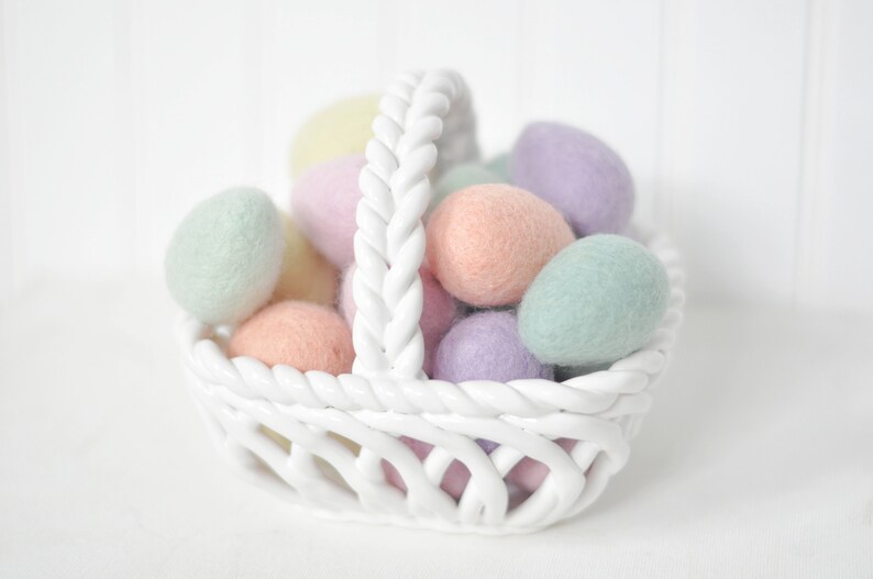 May include: A white ceramic basket filled with pastel colored felt Easter eggs. The basket has a braided rope handle.