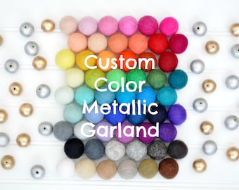 Könnte beinhalten: Ein Regenbogen aus Filzkugeln, die in einem Halbkreis angeordnet sind, mit den Worten "Custom Color Metallic Garland" in weißer Schrift. Die Filzkugeln sind in Reihen verschiedener Farben angeordnet, darunter Rot, Orange, Gelb, Grün, Blau, Lila und Grau. Auf beiden Seiten der Filzkugeln befinden sich auch goldene und silberne Kugeln.