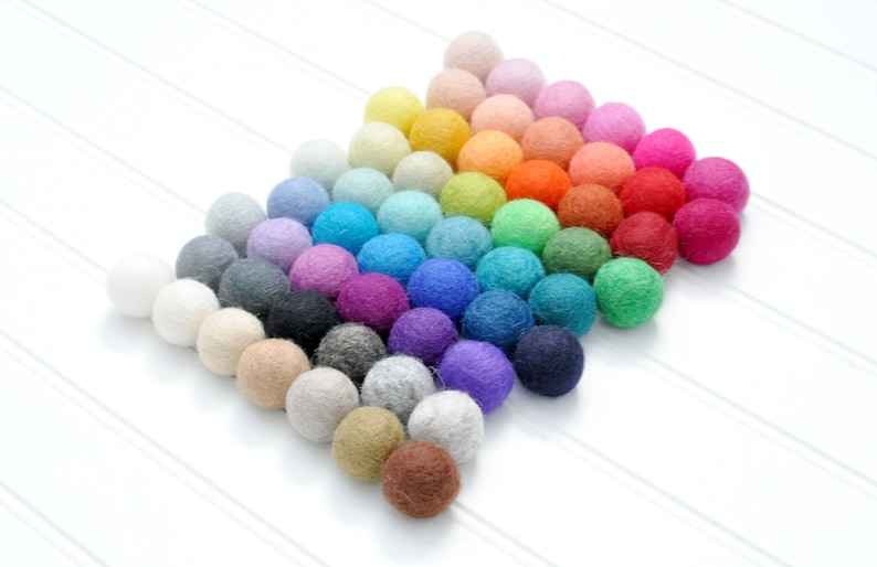 K&ouml;nnte beinhalten: Eine Regenbogen-Sortiment an Filzkugeln, die in Pyramidenform angeordnet sind. Die Kugeln sind in verschiedenen Farben, darunter Rot, Orange, Gelb, Gr&uuml;n, Blau, Lila, Rosa und Braun.